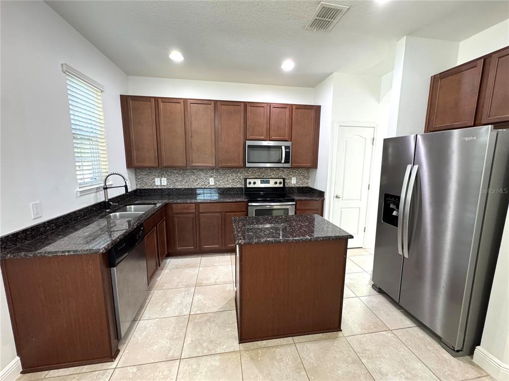 A kitchen features dark wood cabinets, granite countertops, stainless steel appliances, and tile flooring — 12784 GARRIDAN AVENUE, WINDERMERE, FL