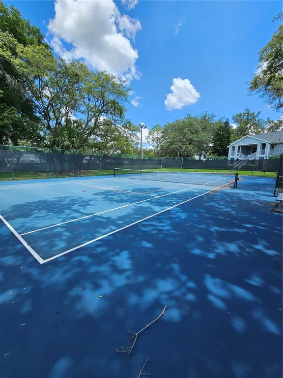 A blue outdoor tennis court with a net, surrounded by a fence and mature trees — 711 SUGAR BAY WAY UNIT 115, LAKE MARY, FL