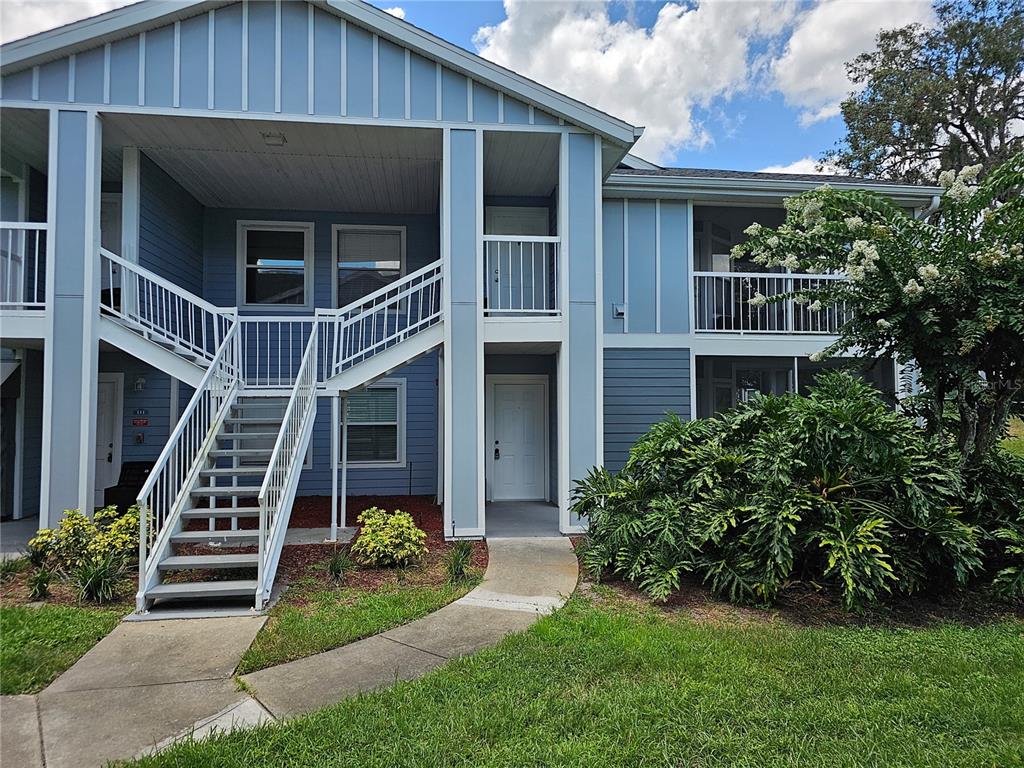 An exterior view of a two-story apartment building with blue siding and an outdoor staircase — 711 SUGAR BAY WAY UNIT 115, LAKE MARY, FL
