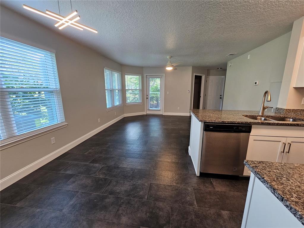 A kitchen with granite countertops and dark tile flooring opens into a living area — 711 SUGAR BAY WAY UNIT 115, LAKE MARY, FL