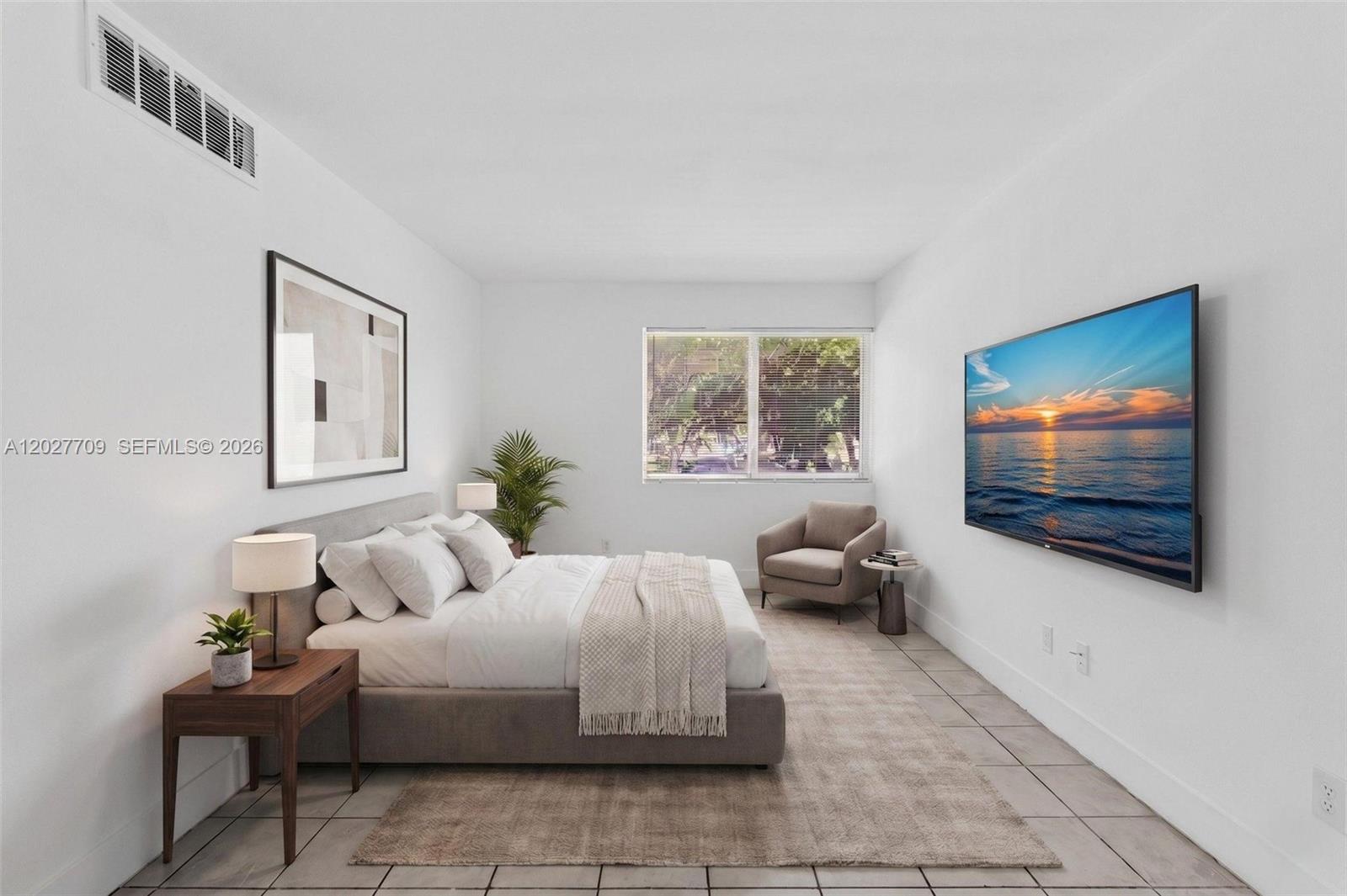 A bedroom features a bed, a wall-mounted television, a window, and a beige armchair — 1000 NW 95th Ter # 103, Miami FL 33150, MIAMI, FL