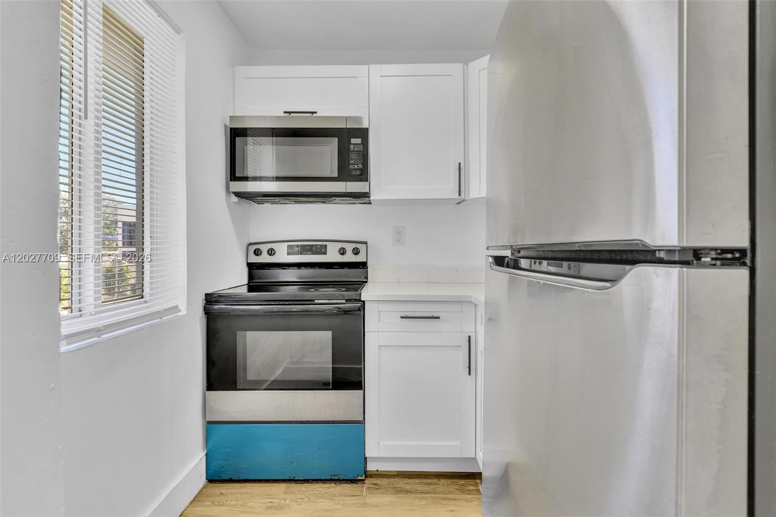 A small kitchen features white cabinets, stainless steel appliances, and a blue-bottomed oven — 1000 NW 95th Ter # 103, Miami FL 33150, MIAMI, FL