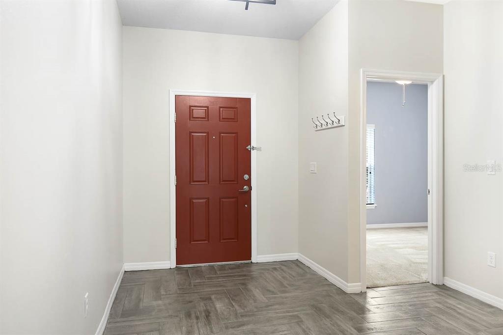 An entryway with gray wood-look flooring, a red front door, and a doorway to another room — 8614 TURNSTONE SHORE LANE, RIVERVIEW, FL