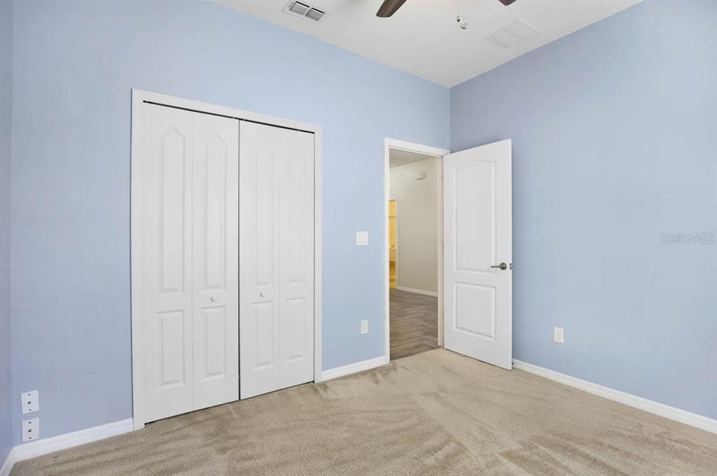 A bedroom with light blue walls, beige carpet, a white closet, and an open doorway — 8614 TURNSTONE SHORE LANE, RIVERVIEW, FL