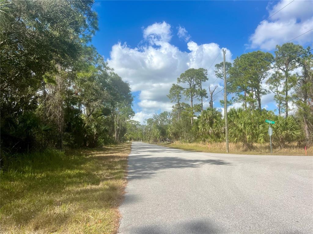 A paved road stretches through a wooded area under a bright, partly cloudy sky — Lot 8 ABBEVILLE ROAD, NORTH PORT, FL