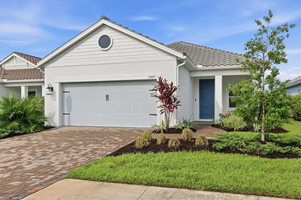 A single-story house with a white stucco exterior, blue front door, and brick paver driveway — 2605 STAR APPLE WAY, SARASOTA, FL