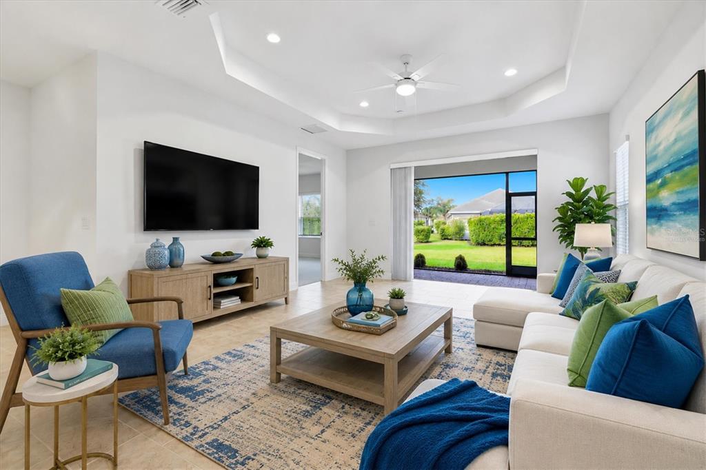 A bright living room features a white sectional, blue armchair, wood coffee table, and television — 2605 STAR APPLE WAY, SARASOTA, FL