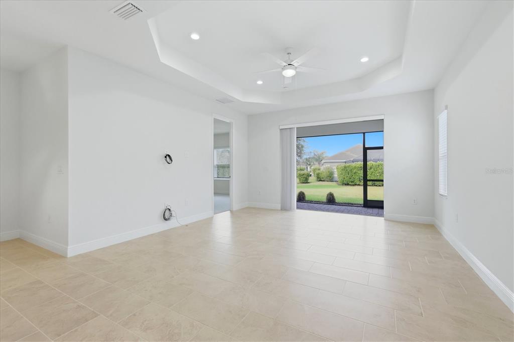A spacious, empty room features white walls, tile flooring, a tray ceiling, and sliding glass doors — 2605 STAR APPLE WAY, SARASOTA, FL