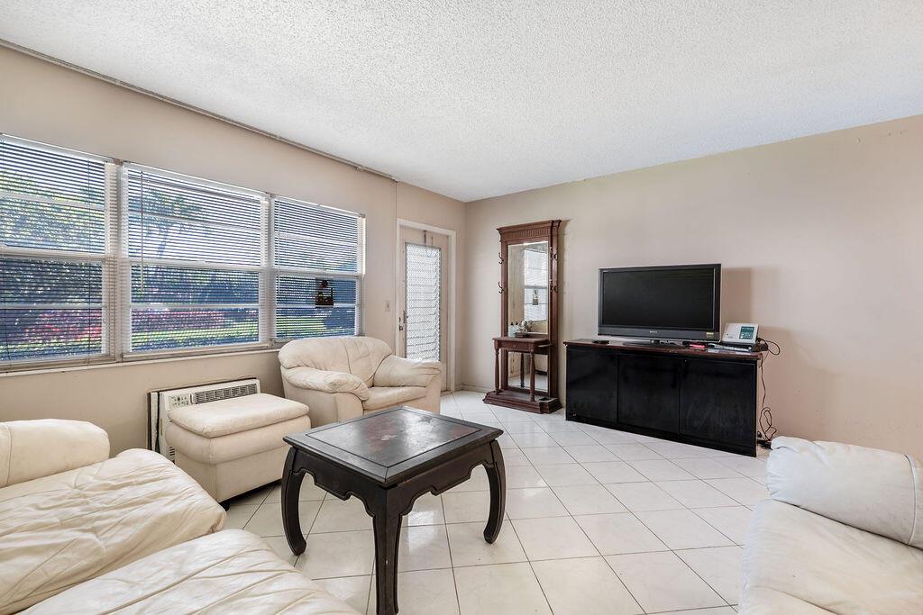A living room with white tile floors, beige walls, white furniture, and a television console — 301 Preston H # 301, Boca Raton FL 33434, BOCA RATON, FL