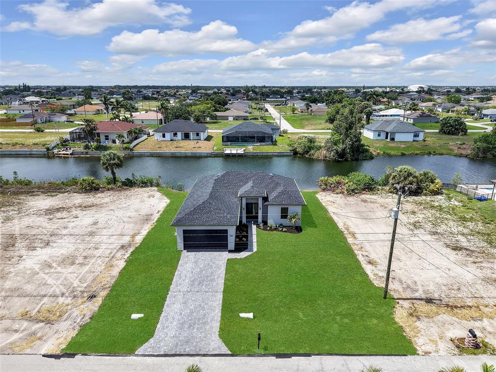 An aerial view shows a single-story house with a paved driveway and a canal backyard — 1505 NW 17TH STREET, CAPE CORAL, FL