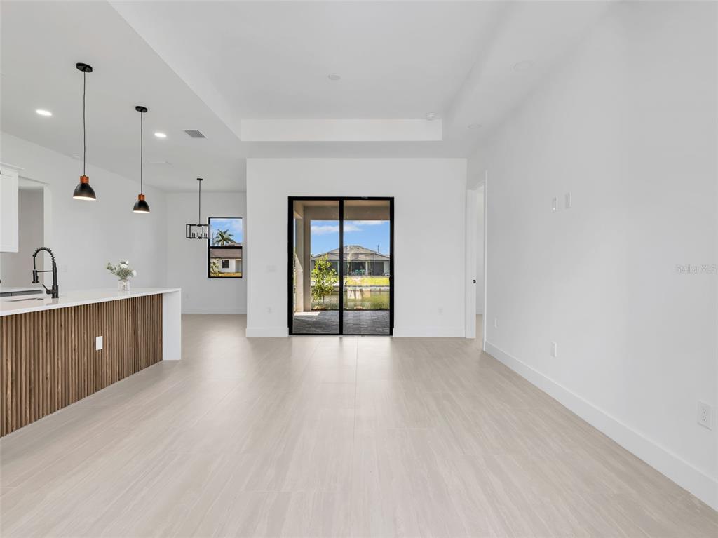 A modern open-concept living area features light wood-look flooring, a kitchen island, and sliding glass doors — 1505 NW 17TH STREET, CAPE CORAL, FL