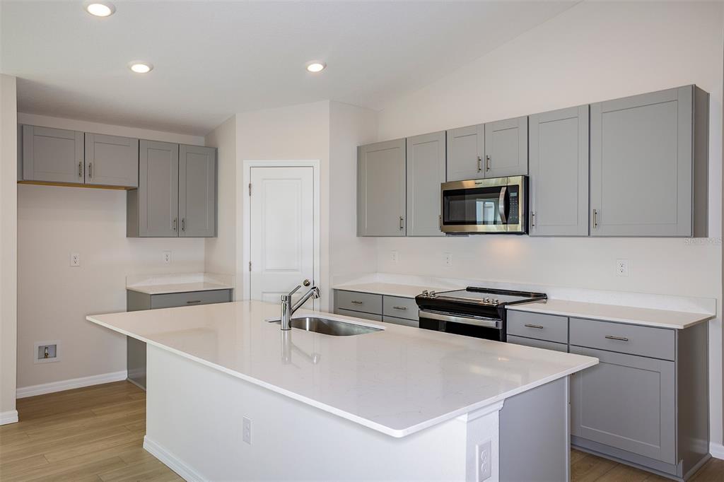 A kitchen features gray cabinets, white countertops, a central island with a sink, and stainless appliances — 31702 OYSTER TRELLIS LANE, WESLEY CHAPEL, FL