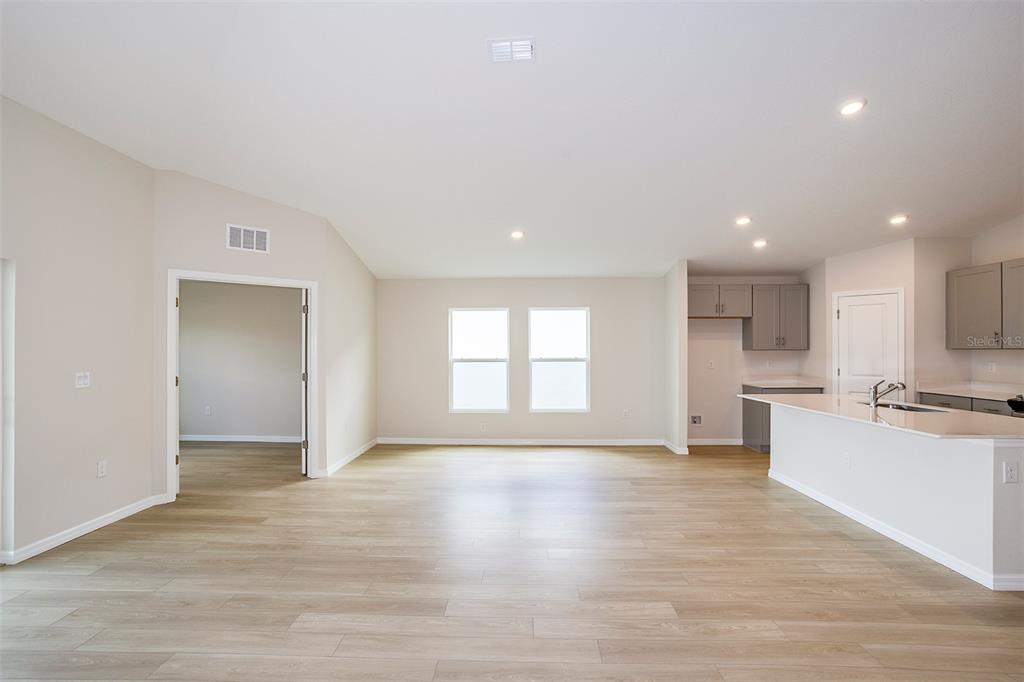 An open-concept living area features light wood-look flooring, neutral walls, and a kitchen island — 31702 OYSTER TRELLIS LANE, WESLEY CHAPEL, FL