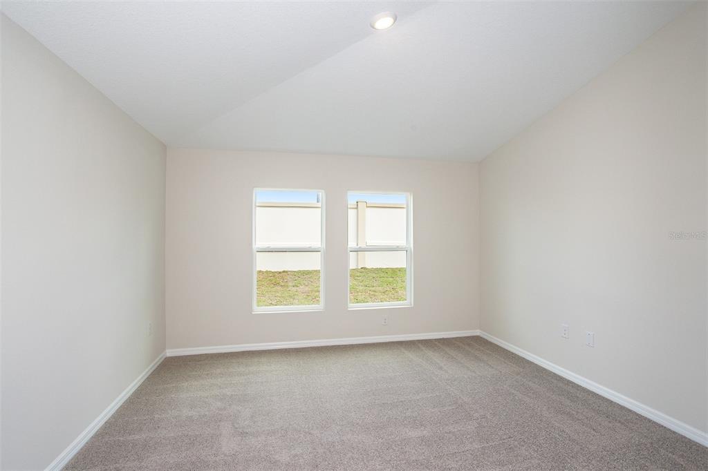 An empty bedroom features beige walls, gray carpeting, and two windows overlooking a concrete wall — 31702 OYSTER TRELLIS LANE, WESLEY CHAPEL, FL