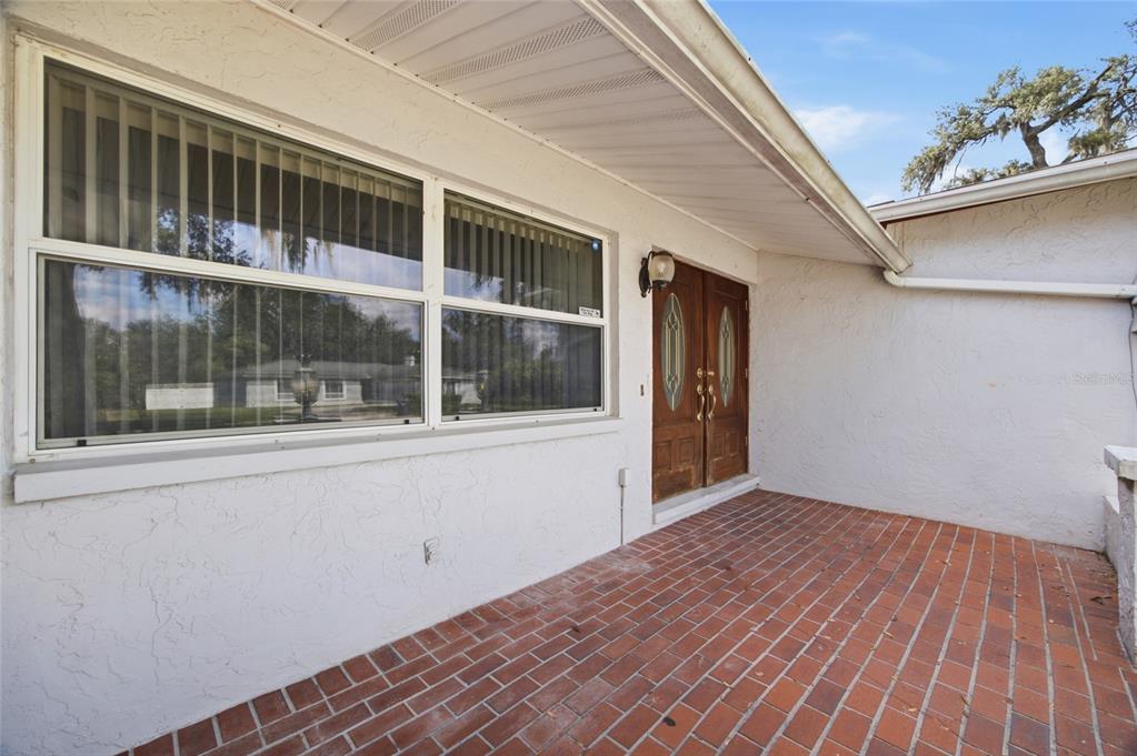 A brick patio leads to a double wooden front door beside a large window — 2969 FOREST CIRCLE, SEFFNER, FL