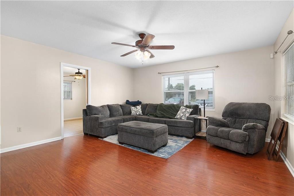 A living room features wood-look flooring, a gray sectional sofa, and a ceiling fan — 1003 DORA AVENUE, TAVARES, FL
