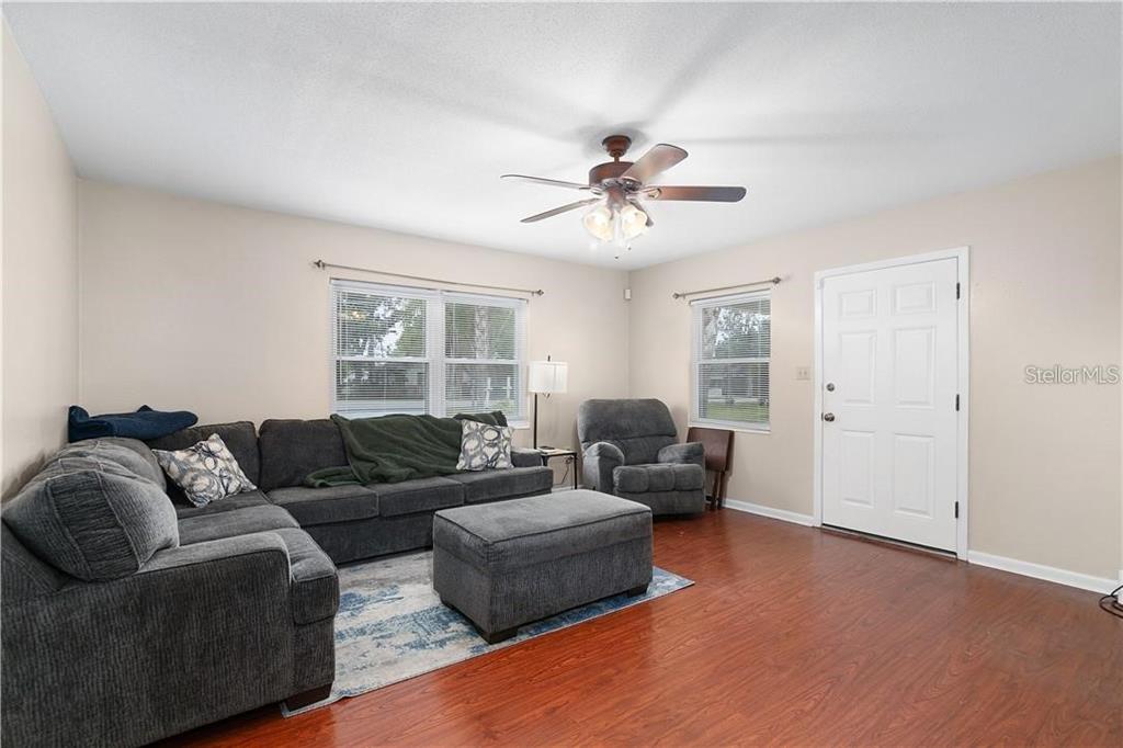 A living room features a gray sectional sofa, matching ottoman, armchair, and wood-look flooring — 1003 DORA AVENUE, TAVARES, FL