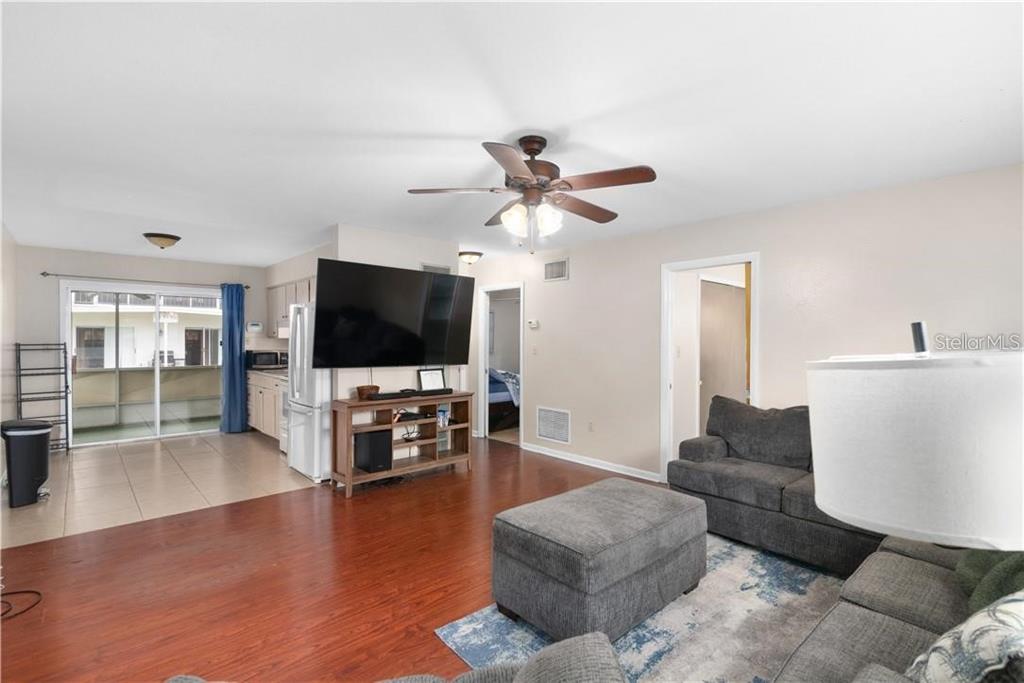 A living room with wood flooring, a large television, and an adjacent kitchen area — 1003 DORA AVENUE, TAVARES, FL