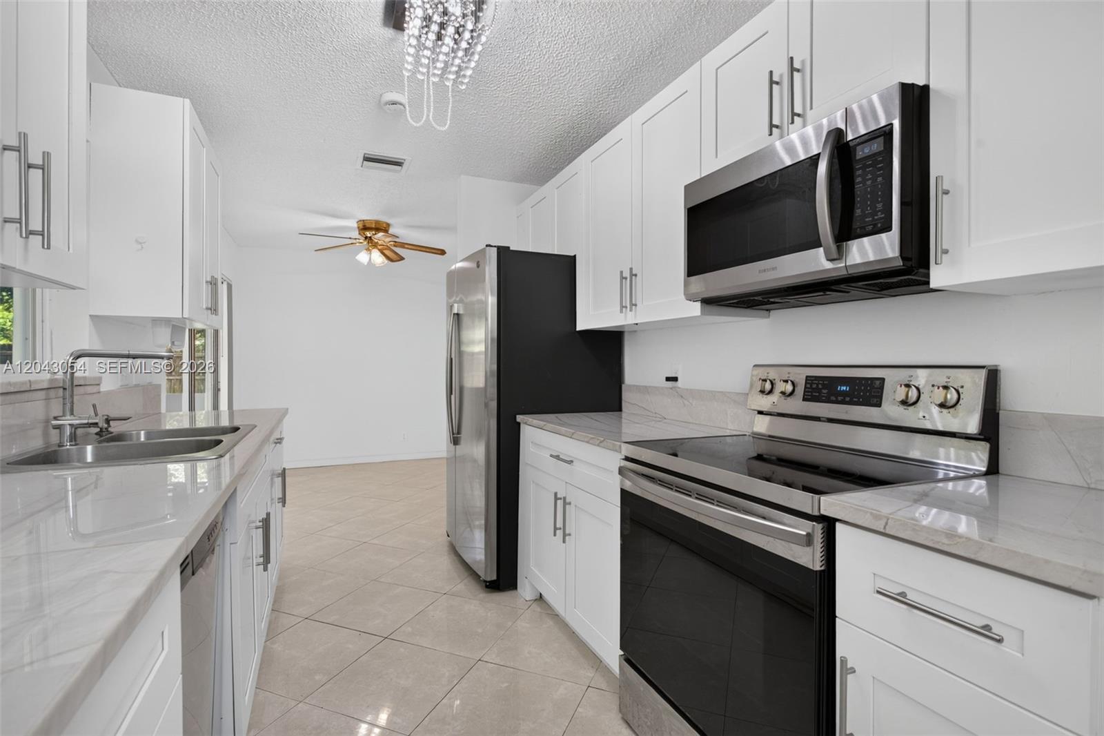 A modern kitchen features white cabinets, stainless steel appliances, and light-colored countertops — 2640 NW 67th Ter, Margate FL 33063, MARGATE, FL