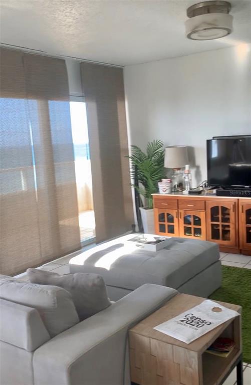 A bright sunroom features white tile flooring, wicker furniture, and large windows overlooking a fenced area — 4939 ISLA VERDE AVE. UNIT 601, CAROLINA, PR