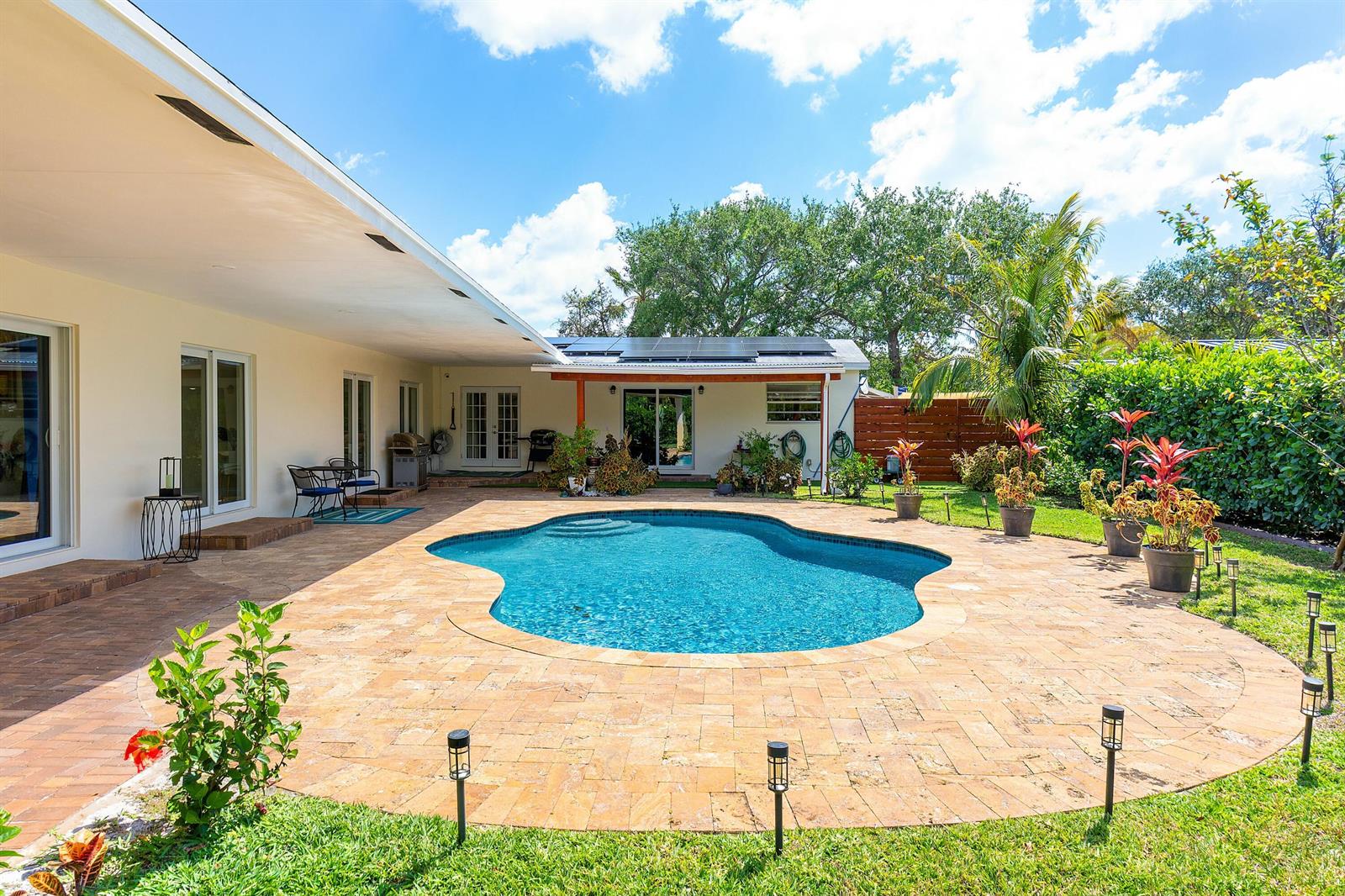 A backyard features a kidney-shaped swimming pool surrounded by a stone patio and landscaping — 1650 NE 3rd Avenue, Delray Beach FL 33444, DELRAY BEACH, FL