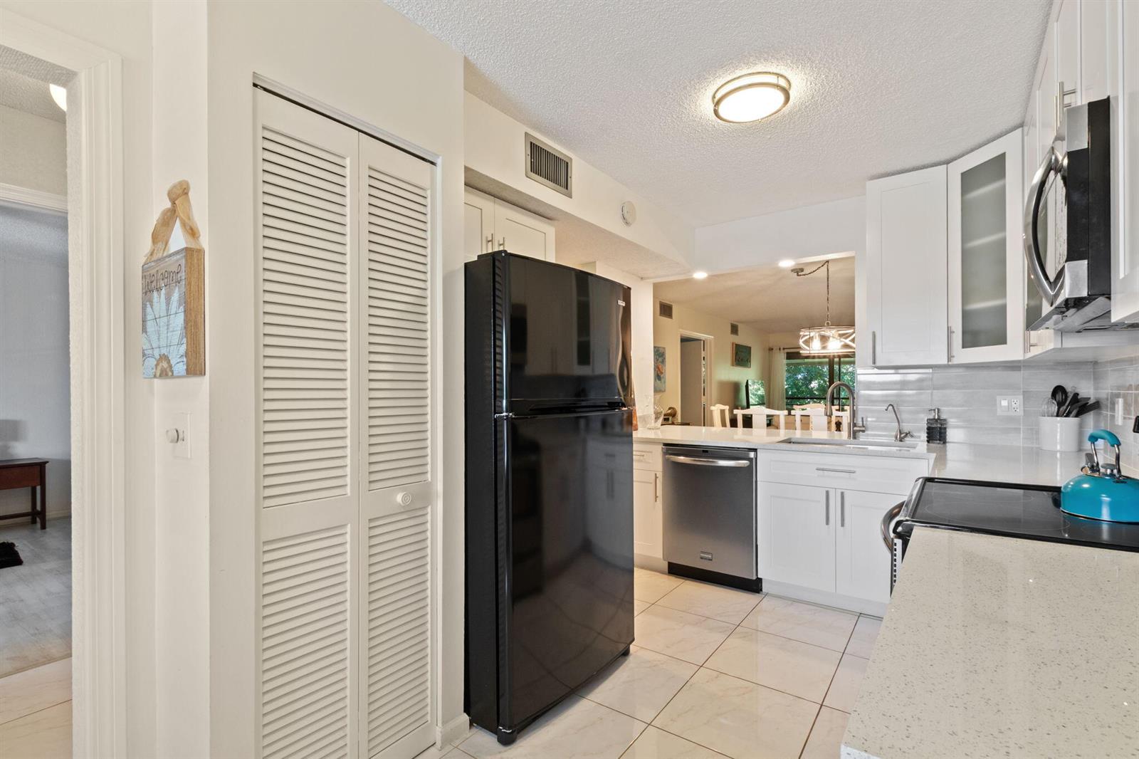 A kitchen with white cabinets, a black refrigerator, stainless steel appliances, and light tile flooring — 5380 Cedar Lake Drive # 304, Boynton Beach FL 33437, BOYNTON BEACH, FL