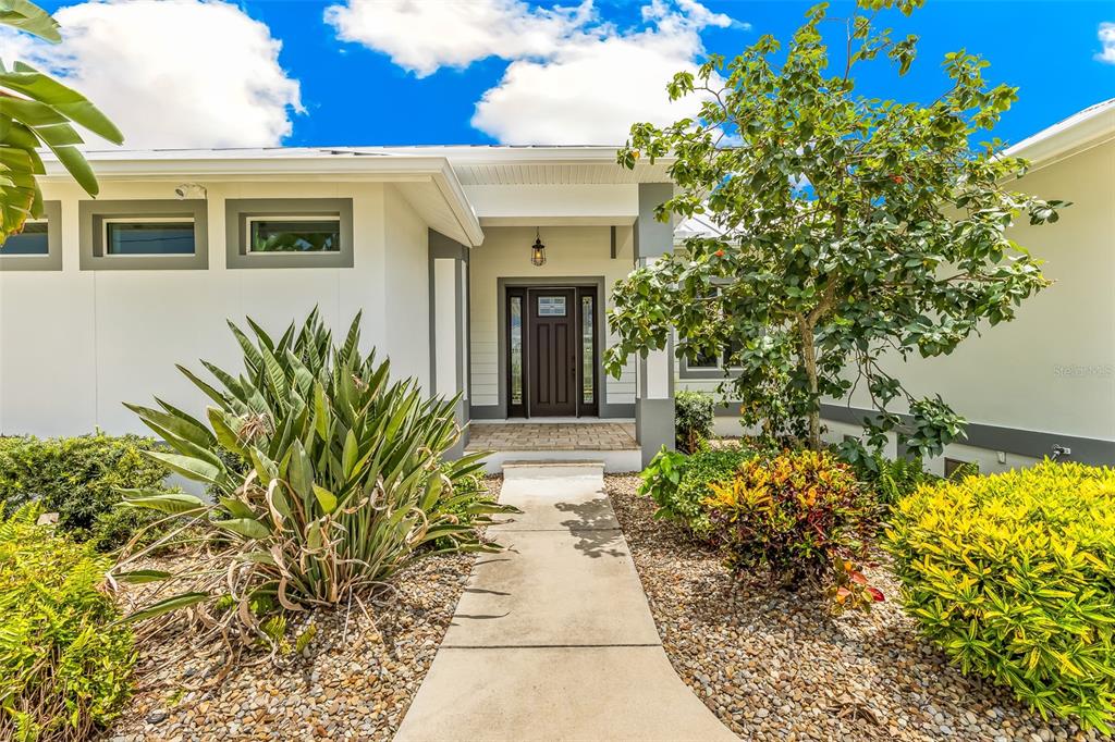 A concrete walkway leads to the dark brown front door of a white modern home — 2477 SIERRA LANE, PUNTA GORDA, FL