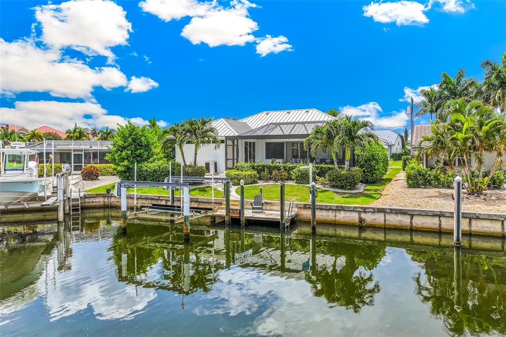 A waterfront house with a boat lift, dock, and screened lanai under a blue sky — 2477 SIERRA LANE, PUNTA GORDA, FL