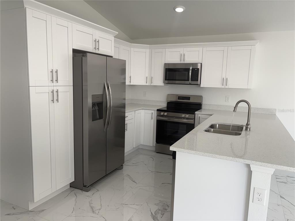 A modern kitchen features white shaker cabinets, stainless steel appliances, and a quartz-topped island — 2810 NW 26TH PLACE, CAPE CORAL, FL