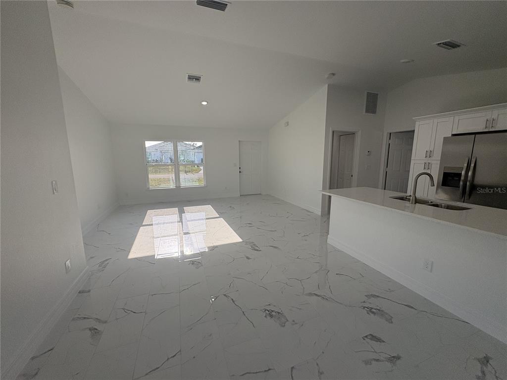 An open-concept living area features white marble-look tile flooring and a kitchen with white cabinets — 2810 NW 26TH PLACE, CAPE CORAL, FL
