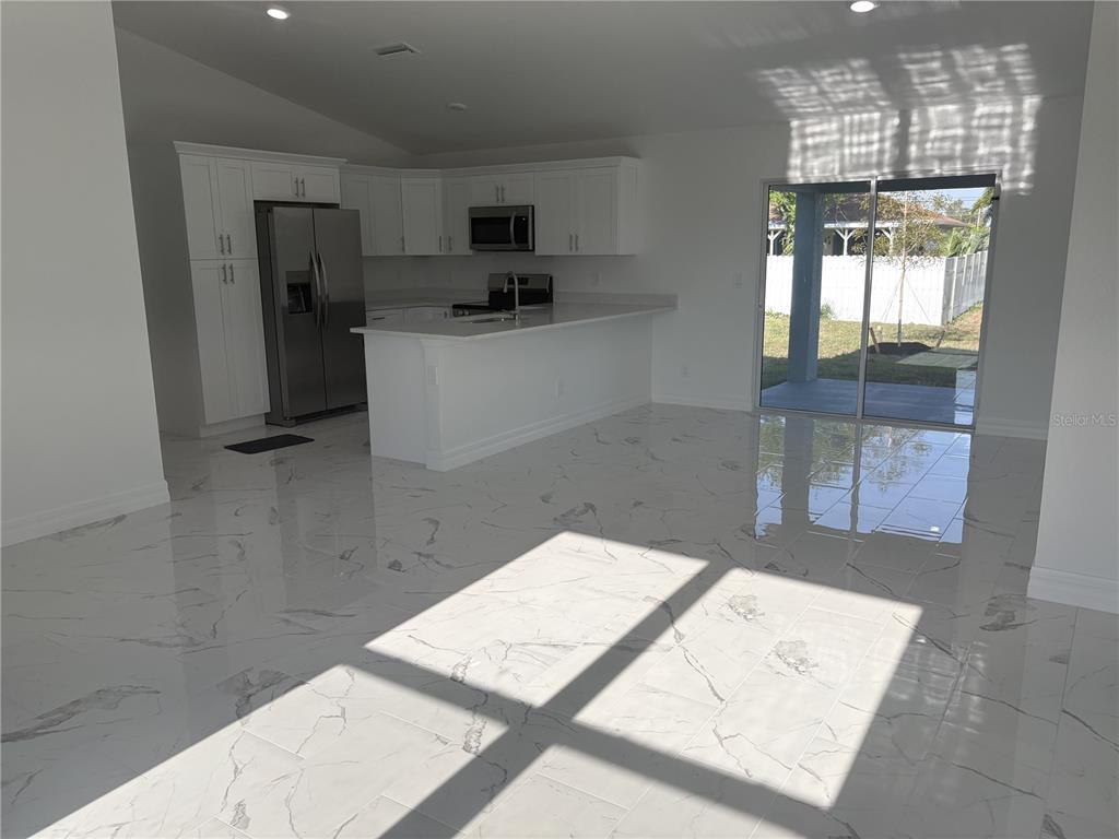 A kitchen with white cabinets and a breakfast bar opens to a tiled living area — 2810 NW 26TH PLACE, CAPE CORAL, FL