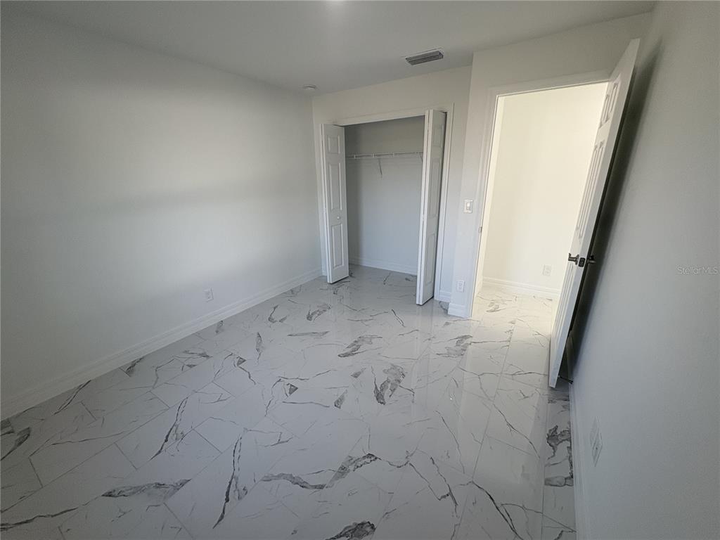 An empty bedroom features white walls, a closet with folding doors, and white marble-patterned flooring — 2810 NW 26TH PLACE, CAPE CORAL, FL