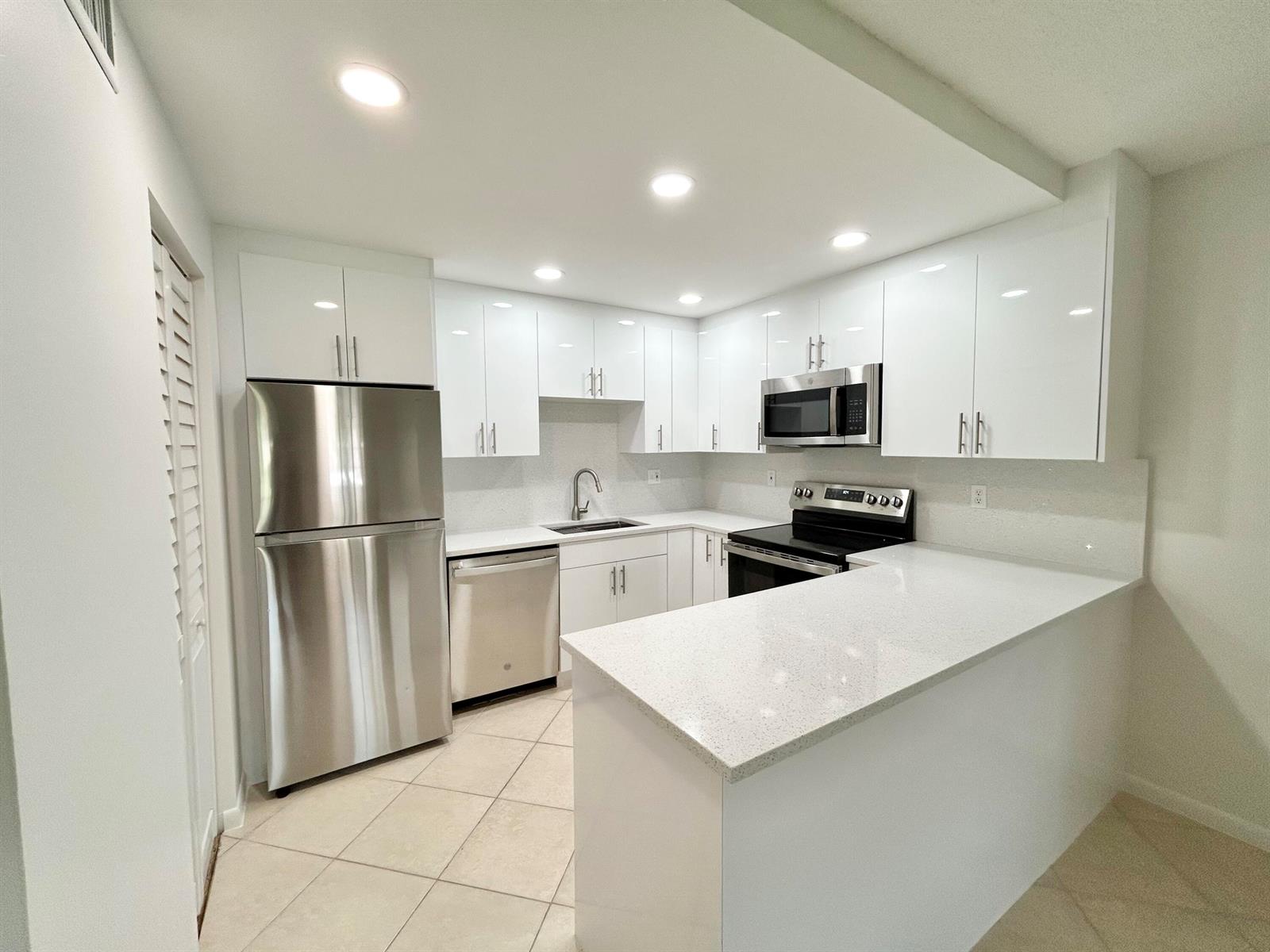 A modern kitchen features white glossy cabinets, stainless steel appliances, and light-colored quartz countertops — 418 Pine Glen Lane # 1, FL 33463, FL