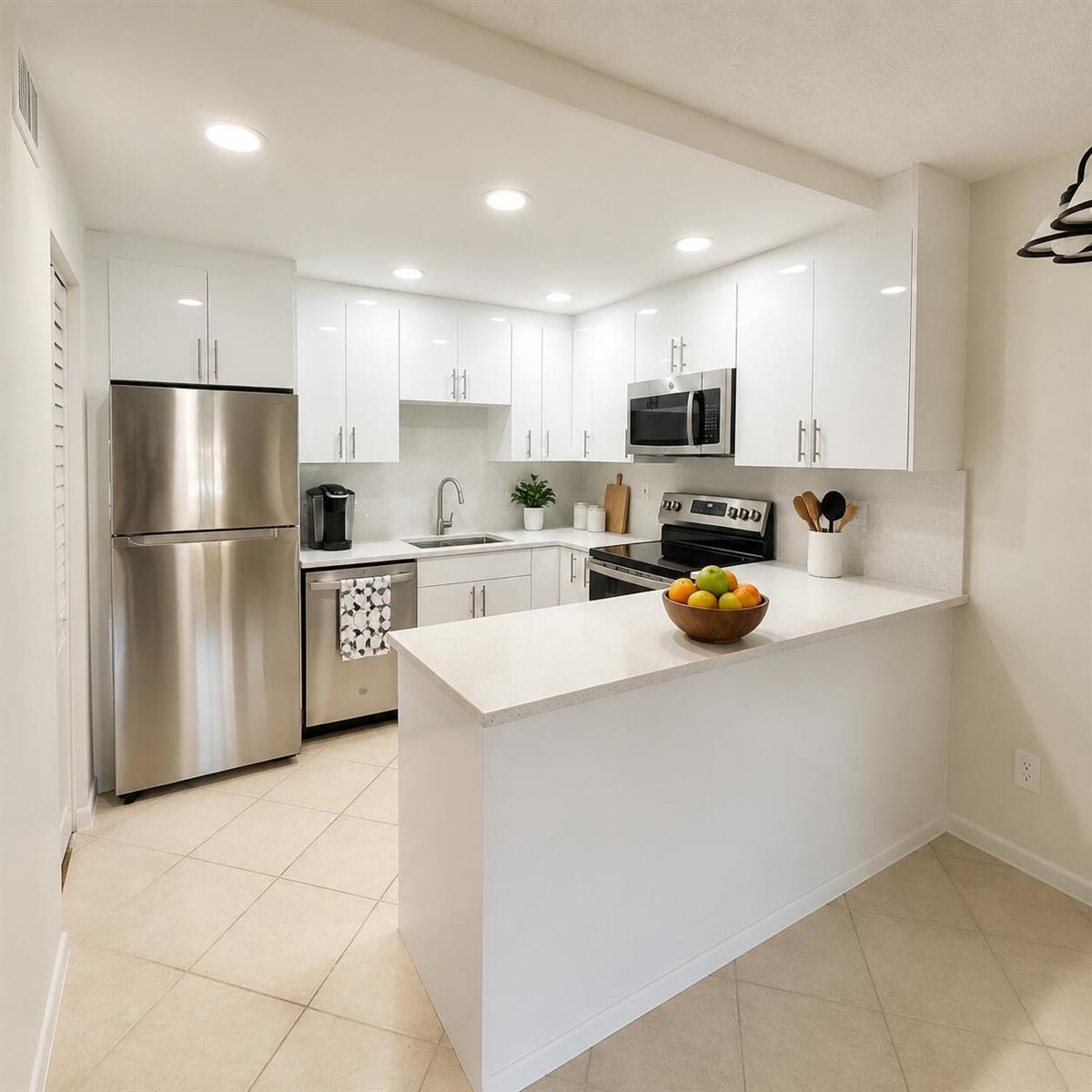 A modern kitchen features white cabinets, stainless steel appliances, and a peninsula with quartz countertops — 418 Pine Glen Lane # 1, FL 33463, FL