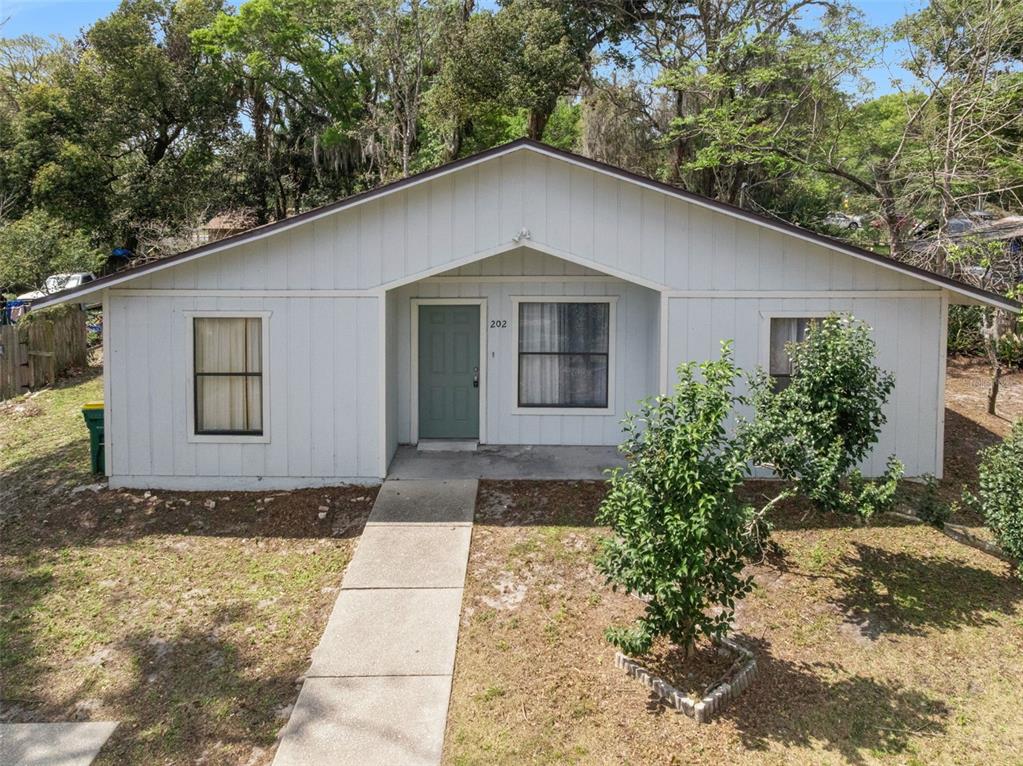 A single-story house with light-colored vertical siding, a green front door, and a concrete walkway — 202 S BOSTON AVENUE, DELAND, FL