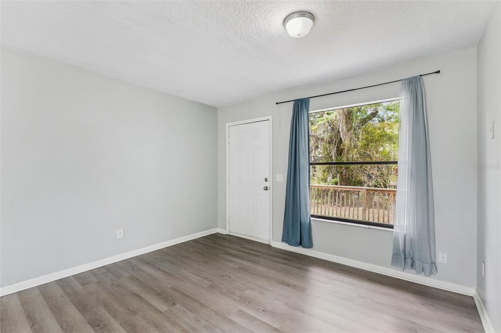 An empty room with light gray walls, wood-look flooring, a white door, and a window — 202 S BOSTON AVENUE, DELAND, FL