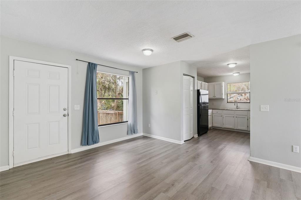 An open-concept living area with light gray walls, wood-look flooring, and an adjacent kitchen — 202 S BOSTON AVENUE, DELAND, FL