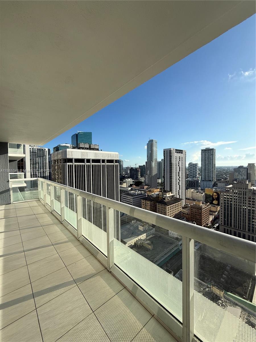 A high-rise balcony with light-colored tile flooring overlooks a dense urban city skyline — 50 Biscayne Blvd # 3405, Miami FL 33132, MIAMI, FL