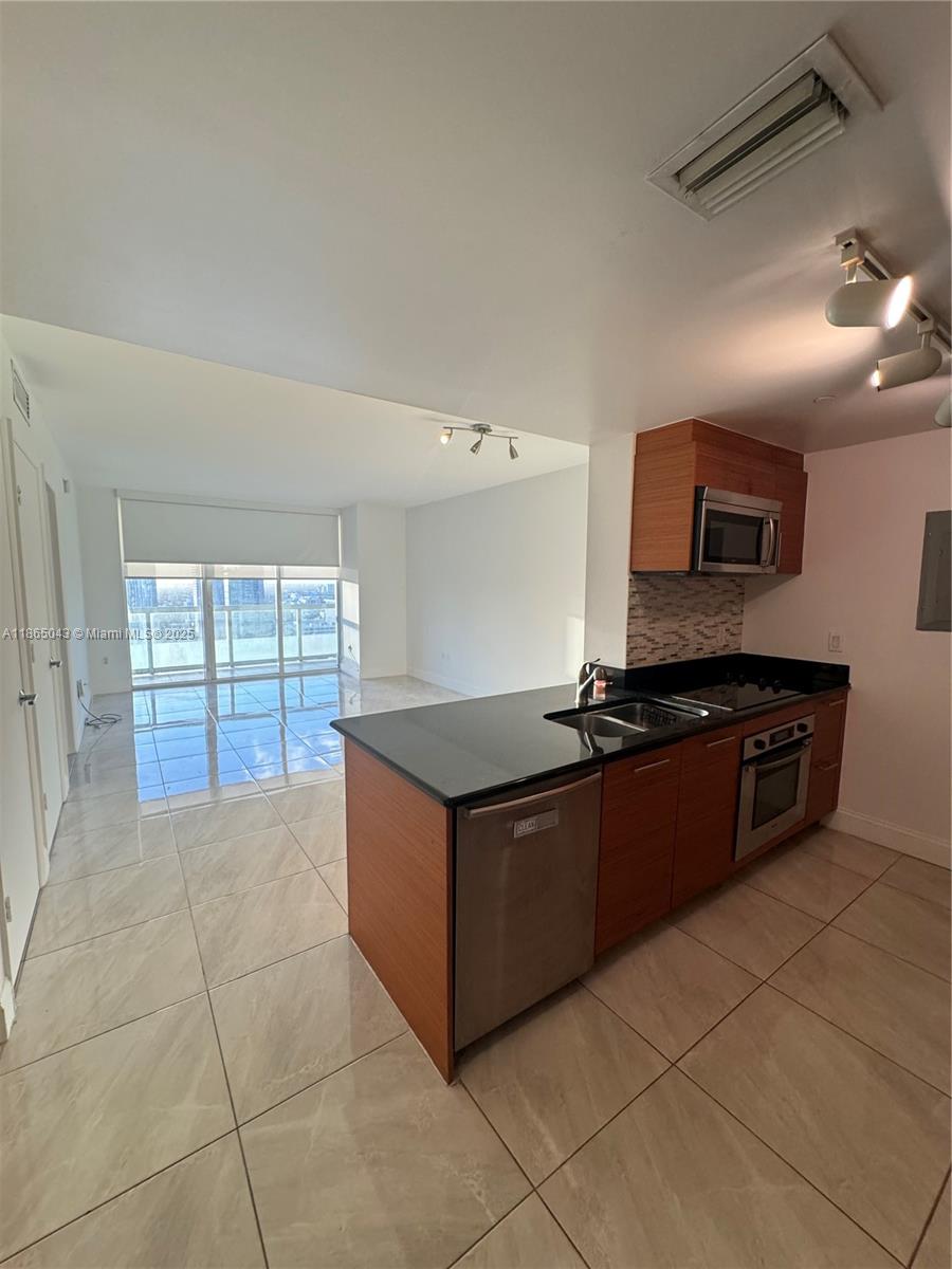 A modern kitchen with wood cabinets and black countertops opens into a bright living area — 50 Biscayne Blvd # 3405, Miami FL 33132, MIAMI, FL