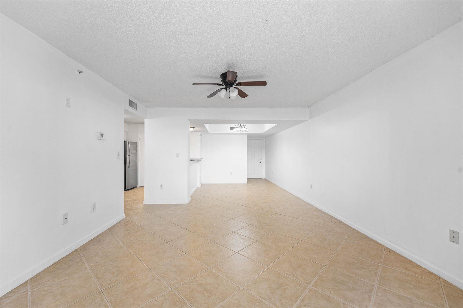 An empty living room features white walls, tan tile flooring, and a ceiling fan — 900 Scotia Drive # 102, Hypoluxo FL 33462, HYPOLUXO, FL