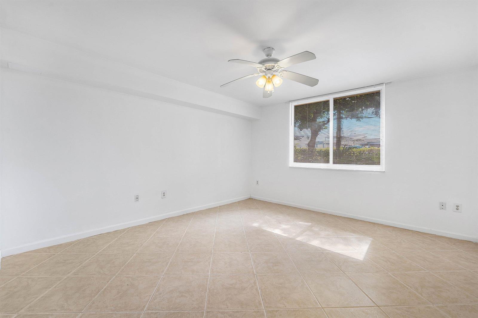An empty room with white walls, beige tile flooring, a ceiling fan, and a window — 900 Scotia Drive # 102, Hypoluxo FL 33462, HYPOLUXO, FL