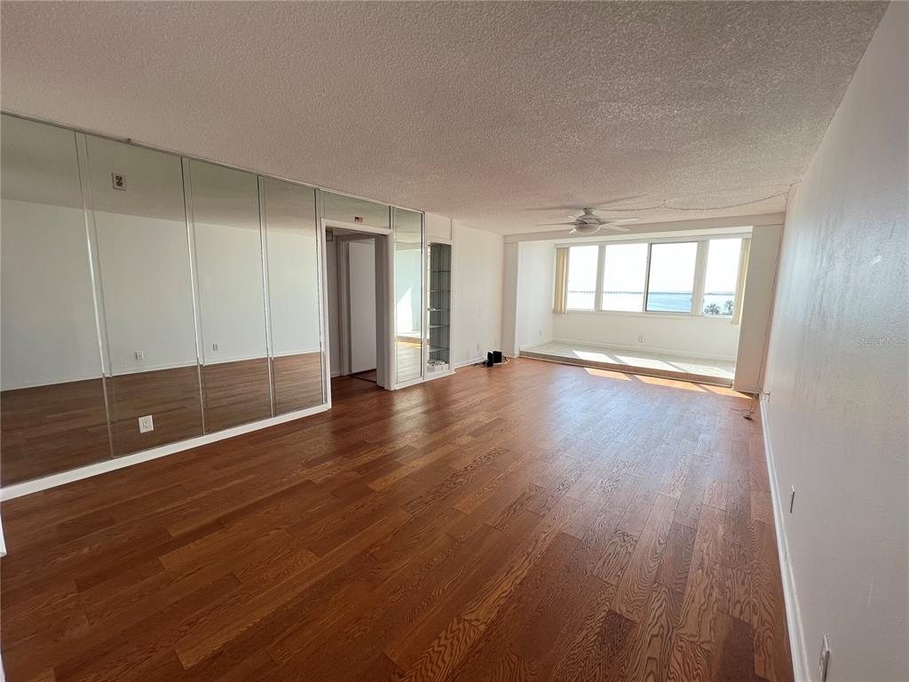 An empty living room features hardwood floors, mirrored wall panels, and a large windowed alcove — 2616 COVE CAY DRIVE UNIT 701, CLEARWATER, FL