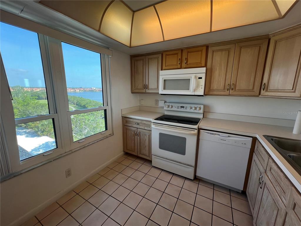 A kitchen with light wood cabinets, white appliances, tile flooring, and a large window view — 2616 COVE CAY DRIVE UNIT 701, CLEARWATER, FL