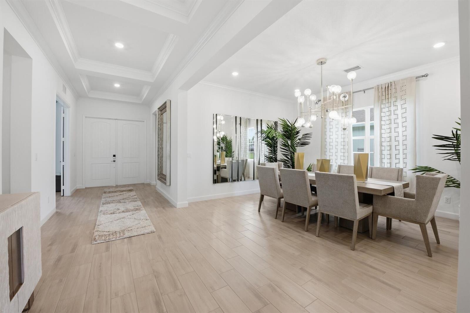 A bright dining room features a modern chandelier, light wood floors, and a large wall mirror — 732 Hookline Circle, Loxahatchee FL 33470, LOXAHATCHEE, FL