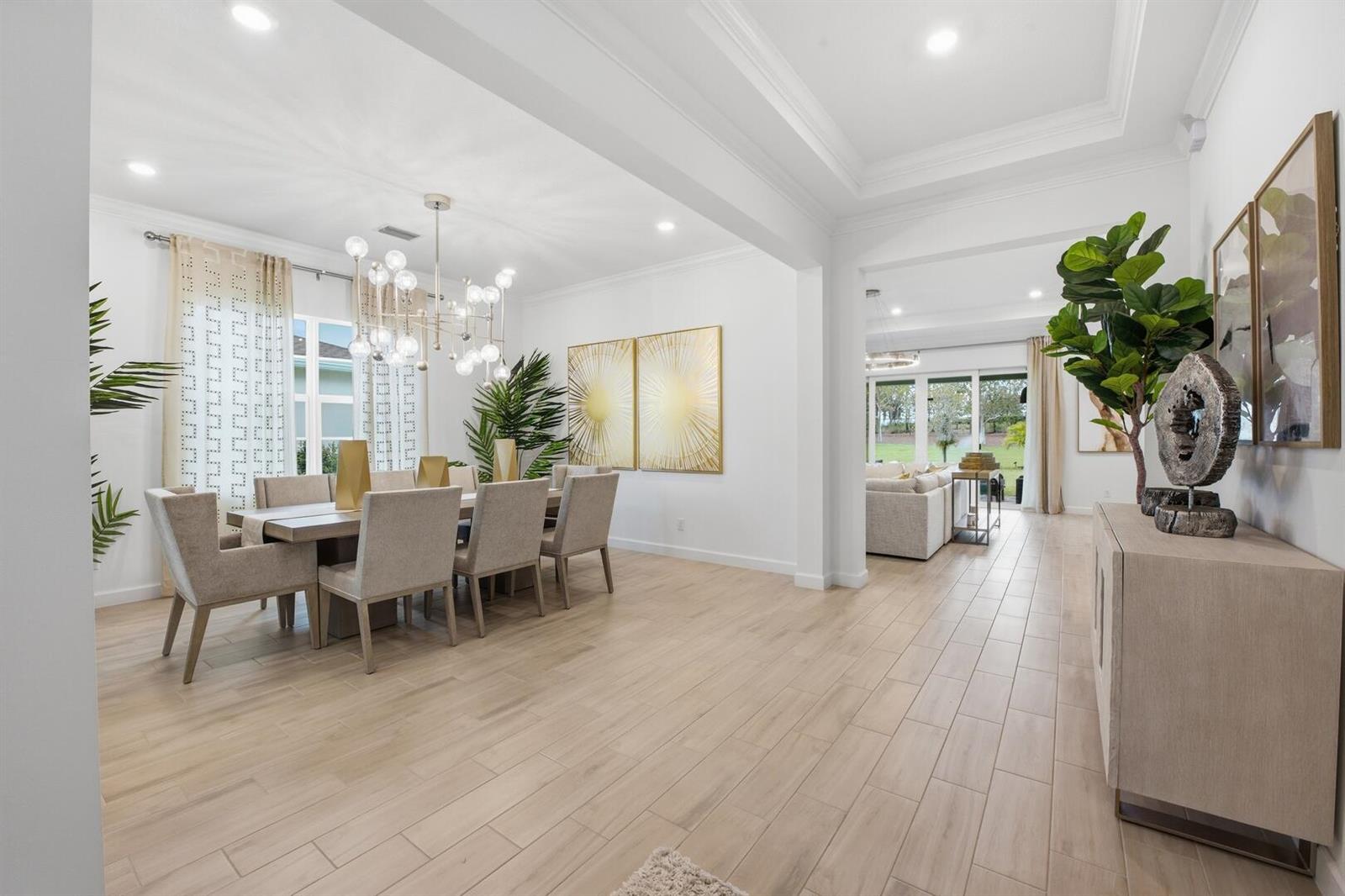 A dining room with a modern chandelier and light wood floors opens to a living area — 732 Hookline Circle, Loxahatchee FL 33470, LOXAHATCHEE, FL