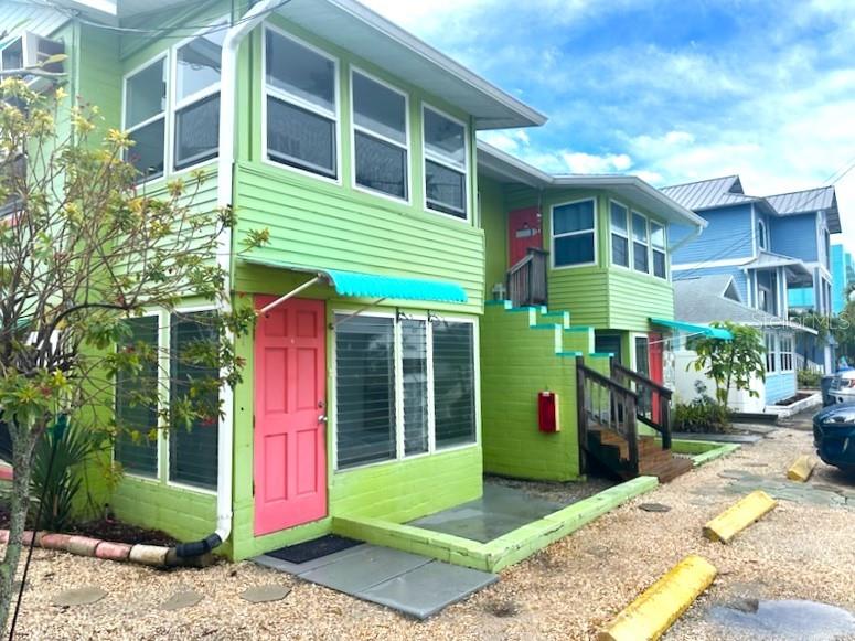 A lime green two-story apartment building features exterior wooden staircases and a bicycle parked underneath — 61 81ST AVENUE UNIT 3, TREASURE ISLAND, FL
