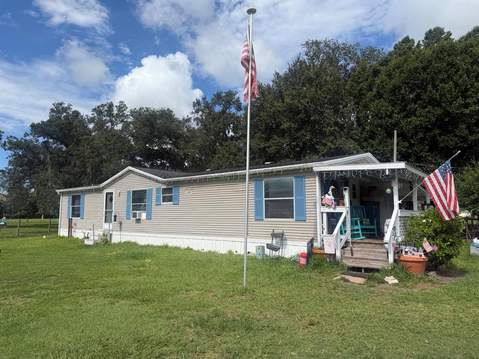 A single-story manufactured home with light siding, blue shutters, a front porch, and a flagpole — 945 NE 28th Avenue, Okeechobee FL 34972, OKEECHOBEE, FL