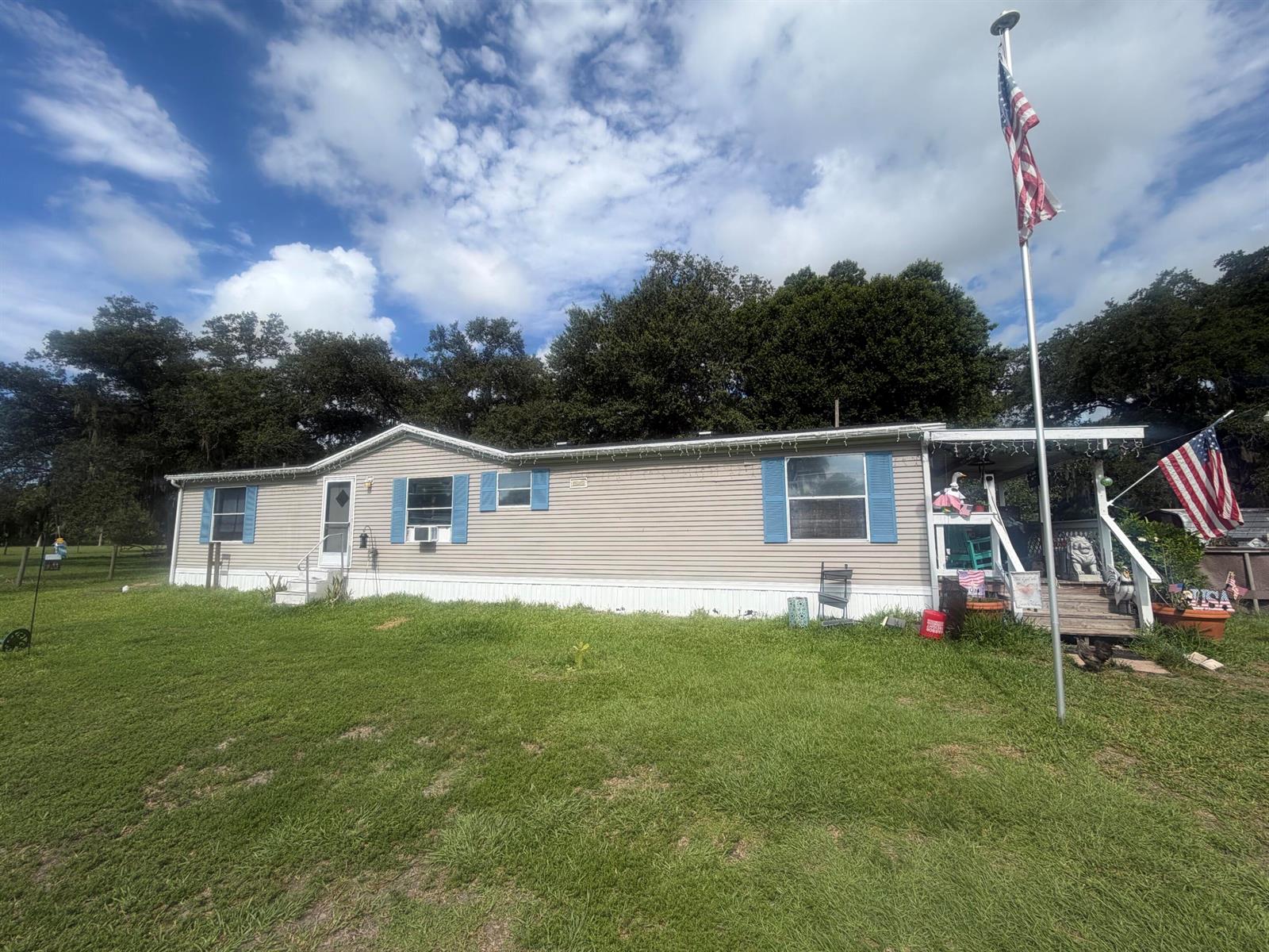 A single-story manufactured home with light siding, blue shutters, and an American flag on a pole — 945 NE 28th Avenue, Okeechobee FL 34972, OKEECHOBEE, FL