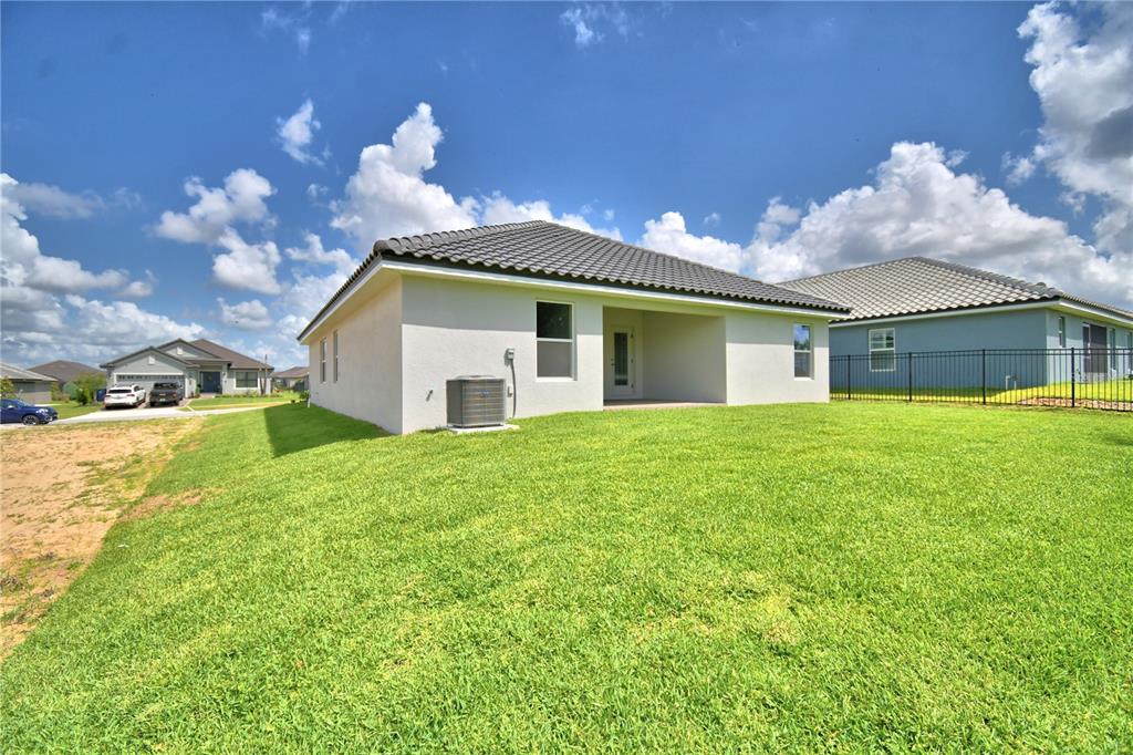 The exterior rear view of a single-story house with a lawn and metal fence — 4514 GRANDVIEW GLEN DRIVE, AUBURNDALE, FL
