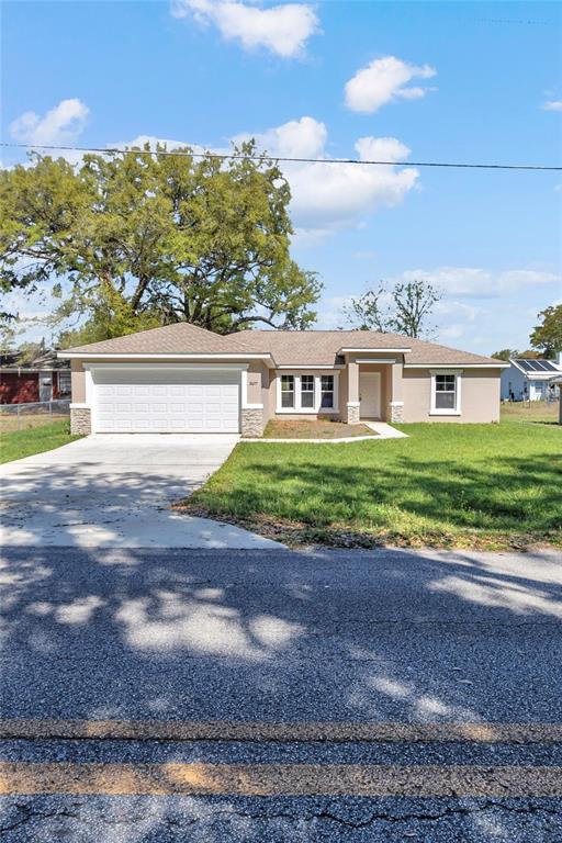 A single-story house with a white garage door, beige siding, and a brown shingled roof — 8677 SE 157TH PLACE, SUMMERFIELD, FL